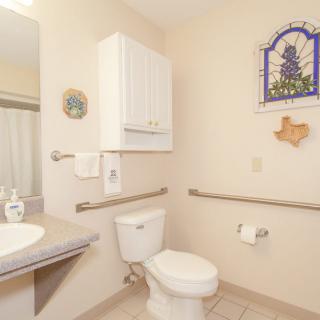 A bathroom with a toilet, sink, and handrails. The room features wall decor and a storage cabinet.