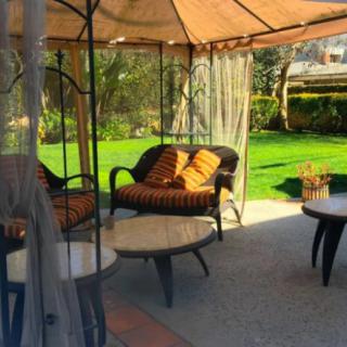 A cozy outdoor patio setup with a gazebo offering shade and comfortable seating, surrounded by a lush green garden.