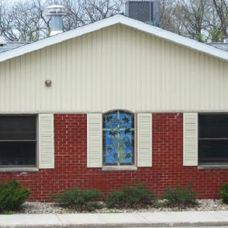 A quaint house featuring a combination of brick and siding with a decorative window.