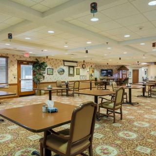 A spacious indoor dining area with several tables and chairs, decorative wall art, and carpeted flooring.