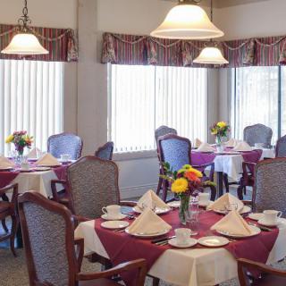 Elegant dining room with tables set for a meal, featuring flowers and folded napkins.