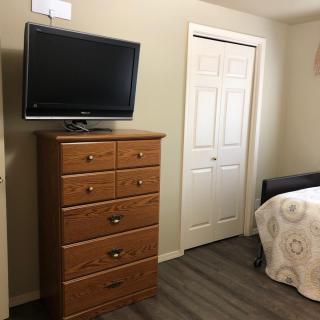 A simple bedroom with a wooden dresser, a mounted TV, and a bed.