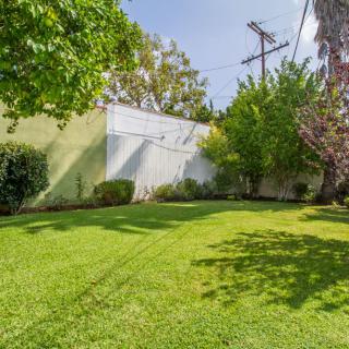 A well-maintained grassy lawn bordered by trees and shrubs under a clear sky.