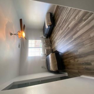 A minimalist bedroom with two twin beds, a ceiling fan, and wood flooring.