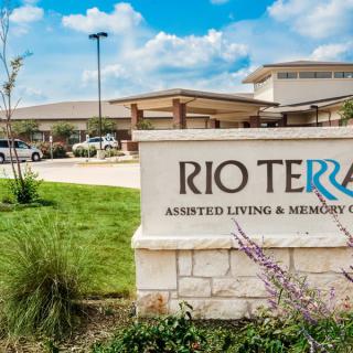 The entrance sign for Rio Terra Assisted Living and Memory Care against a backdrop of the building and landscaped grounds.