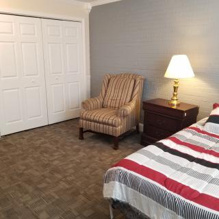 A cozy bedroom with a striped bedspread, an armchair, and a bedside lamp.