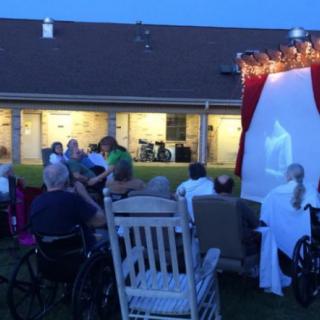 An outdoor evening gathering with people watching a movie projected onto a screen.