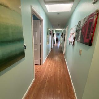 A long hallway with artworks on the walls and a wooden floor, illuminated by overhead lighting.
