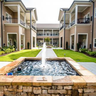 A serene courtyard featuring a central fountain surrounded by well-maintained greenery and modern buildings.