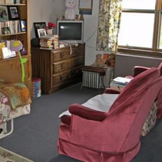 A cozy living room with vintage furniture, including a sofa, chair, and wooden cabinet with a television on top.