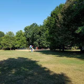 A serene park landscape featuring lush greenery and a sculpture under a clear blue sky.
