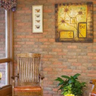 A cozy interior with a brick wall, featuring a wooden chair, vibrant plant, and decorative wall art.