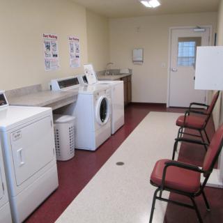 A clean and organized laundry room with washing machines, dryers, and seating.