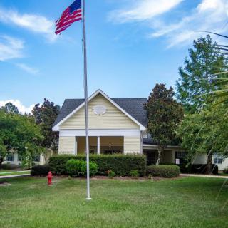 A house with an American flag in the front yard, surrounded by trees and under a clear blue sky.