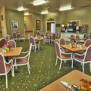 An empty cafeteria with neatly arranged tables and chairs, featuring a carpeted floor and soft lighting.