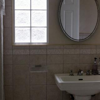 A bathroom with a pedestal sink, round mirror, and tiled walls.
