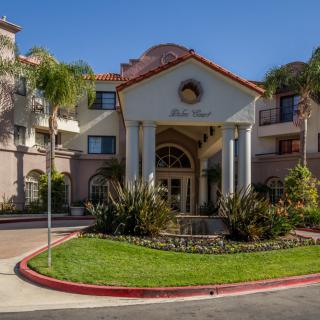 A beautiful building entrance surrounded by landscaped greenery and palm trees under a clear blue sky.