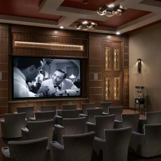 A luxurious home theater with comfortable seating and a black-and-white movie playing on the projector screen.