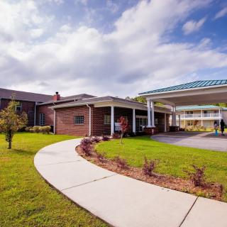 A building with a covered entrance and landscaped pathway under a cloudy sky.