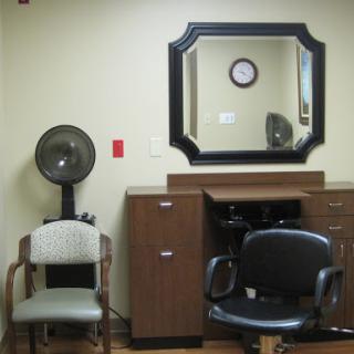 A cozy interior of a salon's waiting area featuring a mirror, clock, and comfortable chairs.