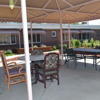 A shaded patio area with tables and chairs, surrounded by a garden.