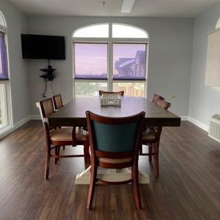 A modern dining room featuring a large table, chairs, and a view through expansive windows.