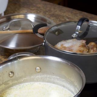 Two pots on a stovetop, one with a creamy liquid and the other with boiling contents, suggesting active cooking in a kitchen.