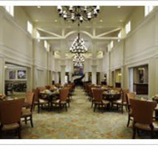 A spacious dining hall with neatly arranged tables and chairs, illuminated by elegant chandeliers.