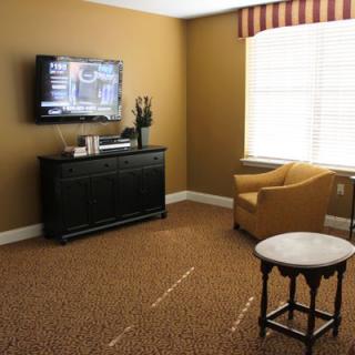 A cozy living room with a wall-mounted television, an armchair, and a small table.