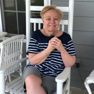 A woman sitting on a porch in a rocking chair, wearing a striped shirt and shorts.