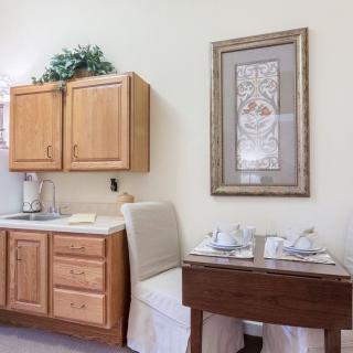 A cozy kitchen corner with wooden cabinets, a small dining table set for two, and framed artwork on the wall.