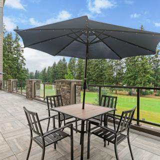 A patio with a table and chairs under an umbrella, overlooking a scenic view of trees.