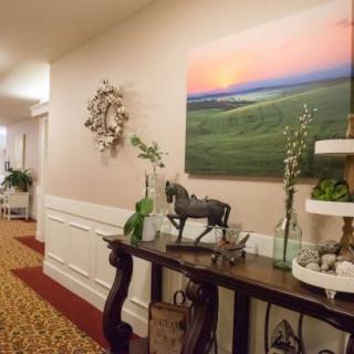 A well-decorated hallway with a side table featuring a horse statue, plants, and artwork on the wall.