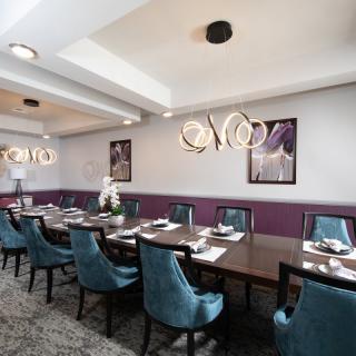 A modern dining room with a long table, blue chairs, and stylish chandeliers.