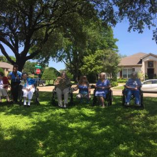 A group of seniors enjoying a sunny day in the park, sitting together on lawn chairs under the shade of a tree.