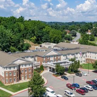 Aerial view of a modern building surrounded by greenery and a parking area.