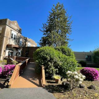 A picturesque view of a garden with vibrant flowers and a charming bridge leading to a building under a clear blue sky.