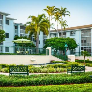 A beautifully landscaped residential area with benches and palm trees in front of an apartment building.