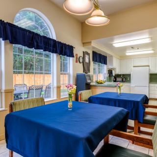 A cozy dining and kitchen area with blue tablecloths and large windows.