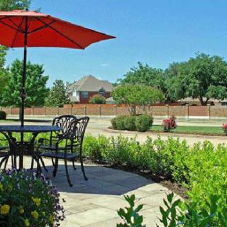 A sunny patio with a table and umbrella overlooking a landscaped garden.