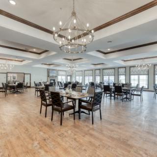 A spacious dining room with elegant chandeliers, arranged tables, and wooden flooring.