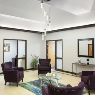 A modern waiting room with purple lounge chairs, a glass coffee table, and minimalist decor.