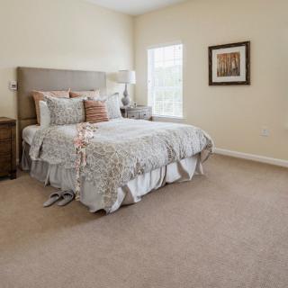A cozy bedroom interior featuring a neatly made bed, carpeted floor, and elegant decor.