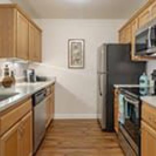 A modern kitchen with wooden cabinets, stainless steel appliances, and wood flooring.
