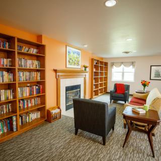 A cozy library room with bookshelves and a seating area around a fireplace.
