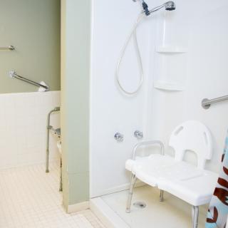 An accessible bathroom with a shower area equipped with grab bars and a shower chair for safety.