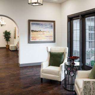 A cozy living room with armchairs, a scenic painting, and large windows providing natural light.