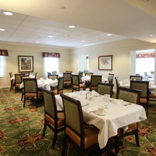 A well-arranged dining area with tables and chairs set for service, featuring elegant decor and a carpeted floor.