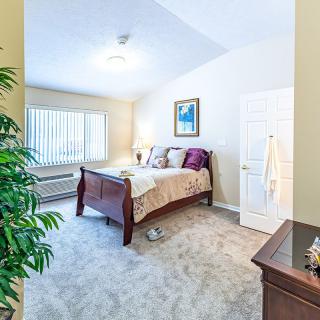 A cozy bedroom with a wooden bed, plush carpet, and natural light from a large window.