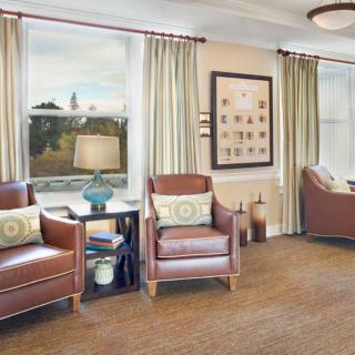 A cozy living room with leather chairs, large windows, and a lamp on a side table.
